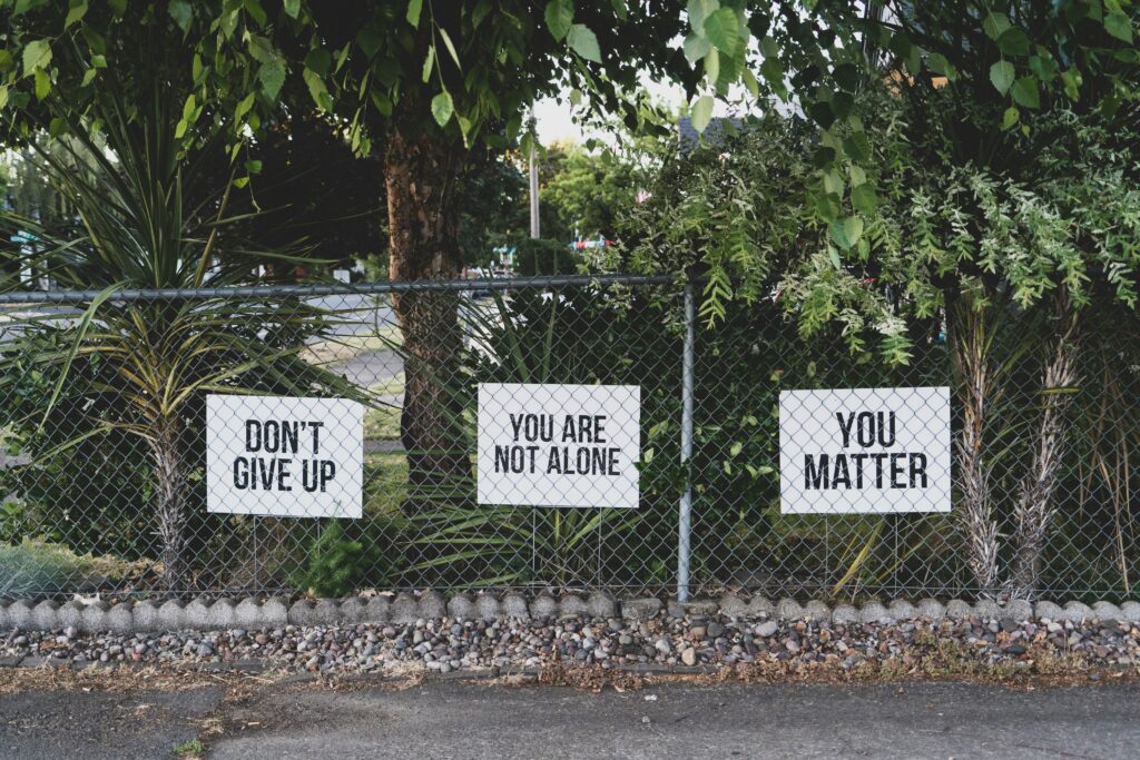 Signs on a fence saying “You are not alone” and “Don’t give up”